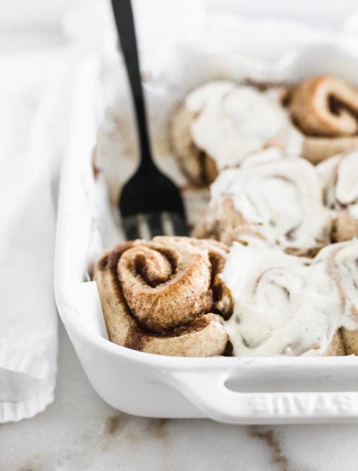 cinnamon rolls in a white baking dish with a black fork in the background.