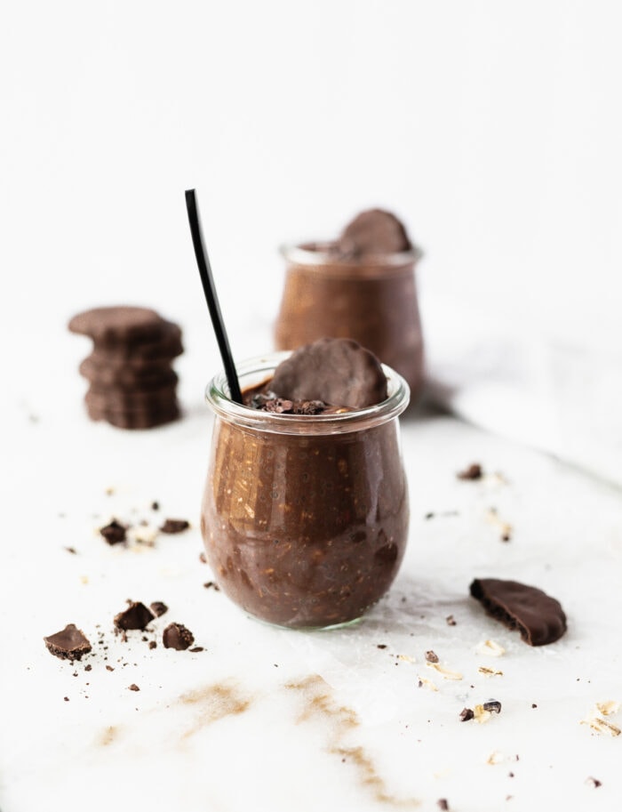 thin mint overnight oats in a glass jar with a black spoon and a thin mint cookie in the top.