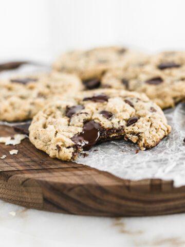 oatmeal chocolate chip cookie with a bite taken out on a wooden board with more cookies in the background.