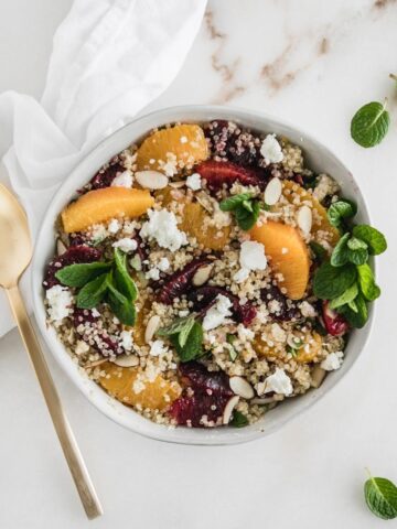 overhead view of quinoa salad with blood oranges, navel oranges, mint and goat cheese in a bowl with a gold fork beside it.