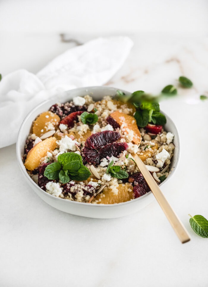 Blood orange quinoa salad in a bowl with a gold spoon in it.
