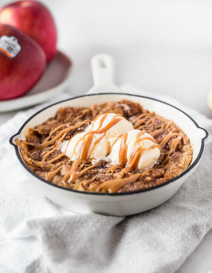 chickpea apple snickerdoodle skillet cookie in a white skillet topped with ice cream and caramel sauce.