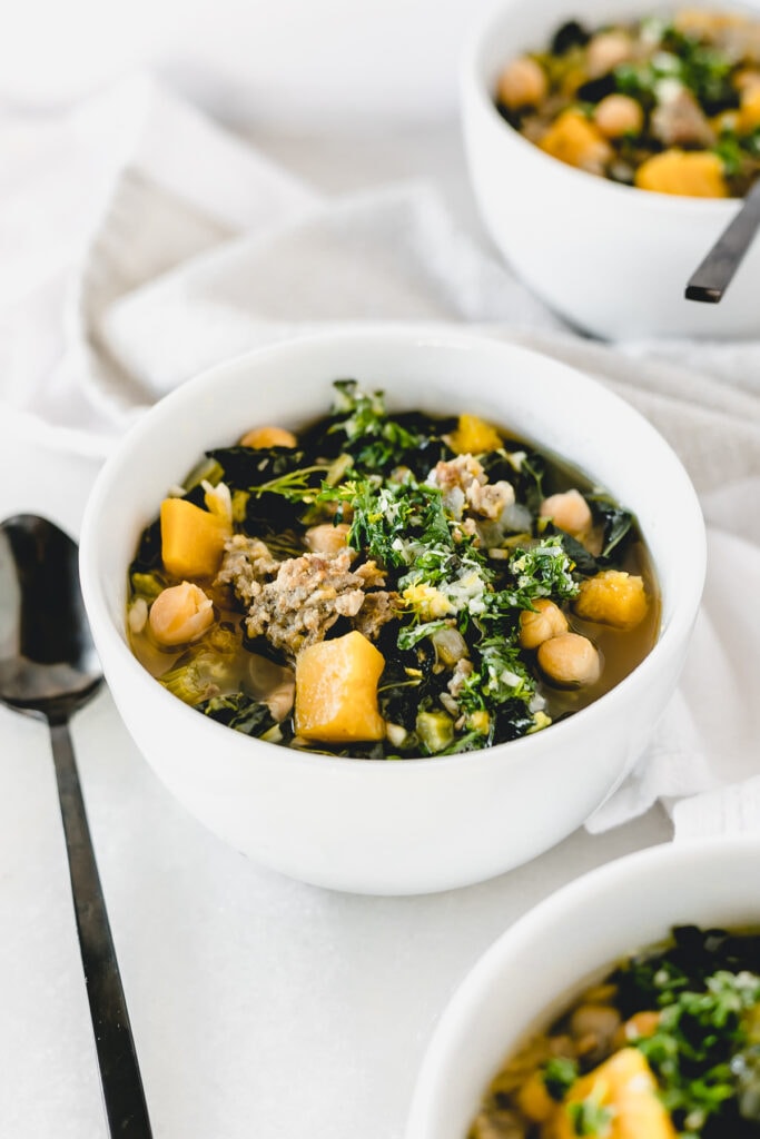 kale sausage butternut squash soup in a white bowl with a black spoon next to it.