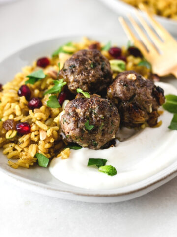 three lamb meatballs on top of jeweled rice and yogurt on a small grey plate.