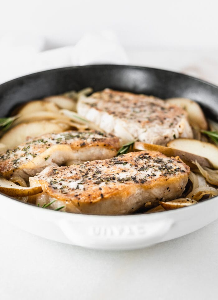 rosemary crusted pork chops with pears and onions in a white cast iron skillet.