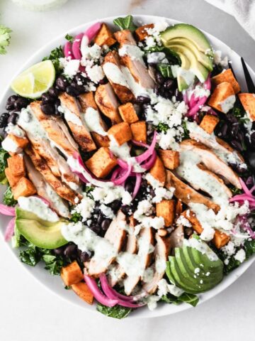 overhead view of smoky grilled chicken and sweet potato kale salad drizzled with creamy dressing on a large plate with a black fork.