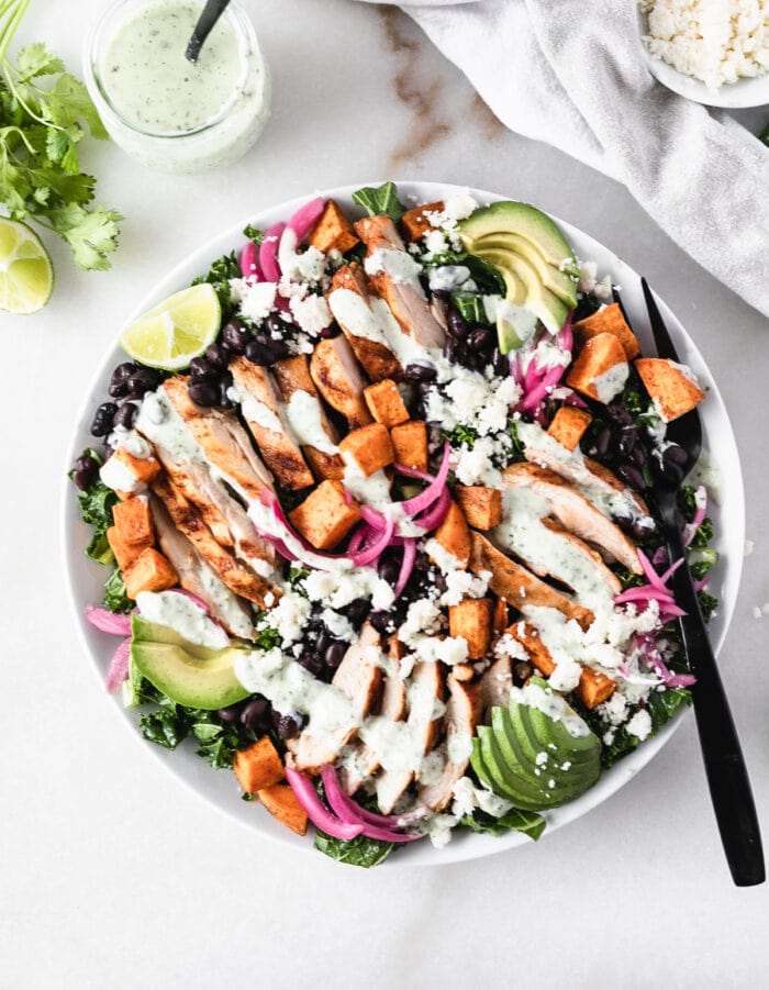 overhead view of smoky grilled chicken and sweet potato kael salad drizzled with creamy dressing on a large plate with a black fork.