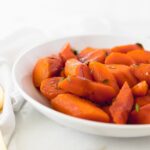 closeup of carrots in a white bowl with thyme and balsamic glaze.