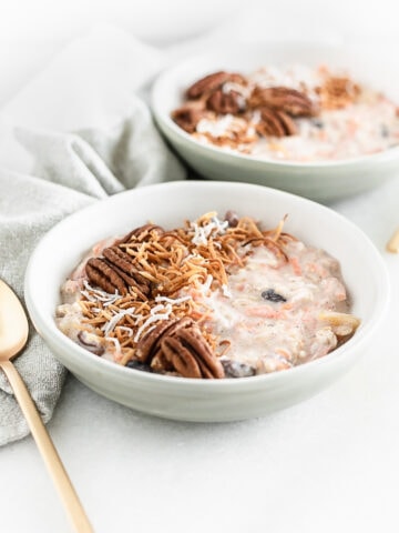 bowl of carrot cake overnight oats topped with toasted pecans and coconut flakes with a gold spoon beside it.
