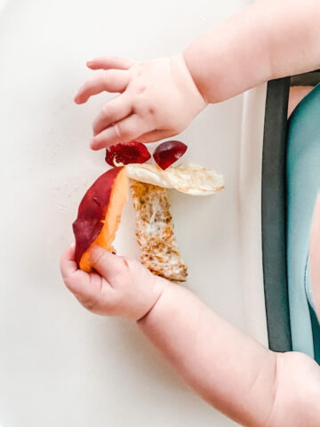 overhead view of a baby's hands picking up pieces of food on a high chair tray.