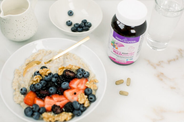 bowl of oatmeal topped with berries and walnuts with a bottle of postnatal vitamins next to it.