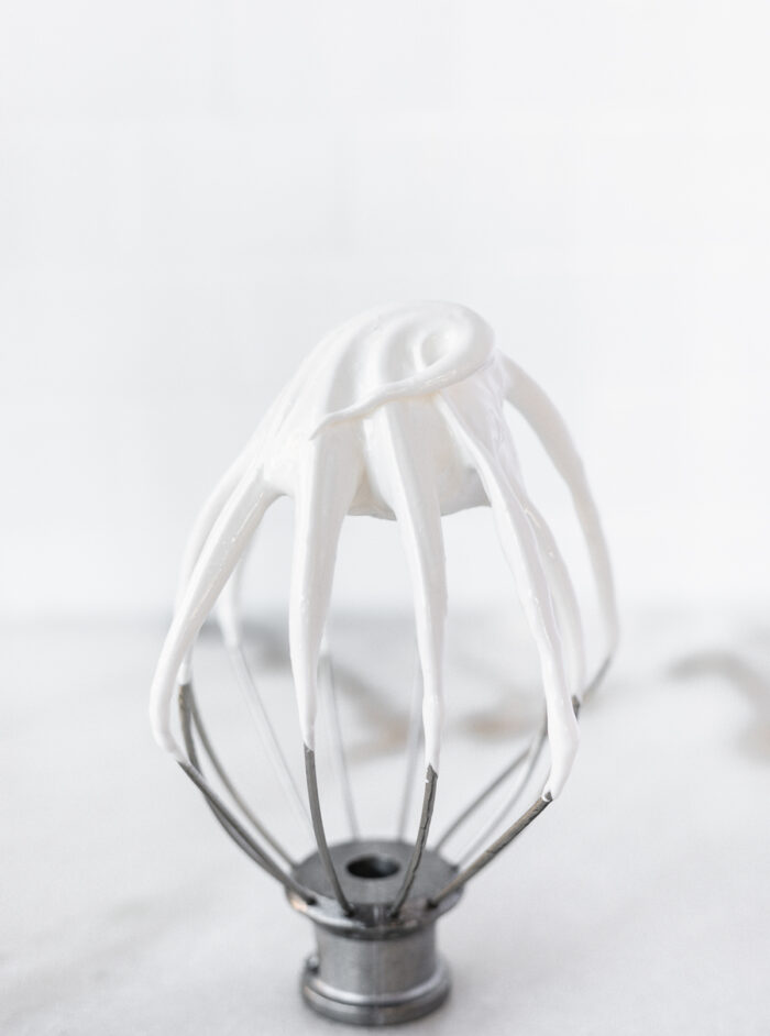 stand mixer whisk with 7 minute frosting on it standing against a marble background.