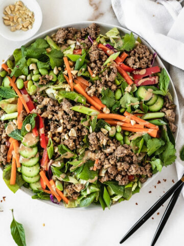 overhead view of thai ginger ground beef salad with a bowl of chopped peanuts and two gold and black forks beside it.