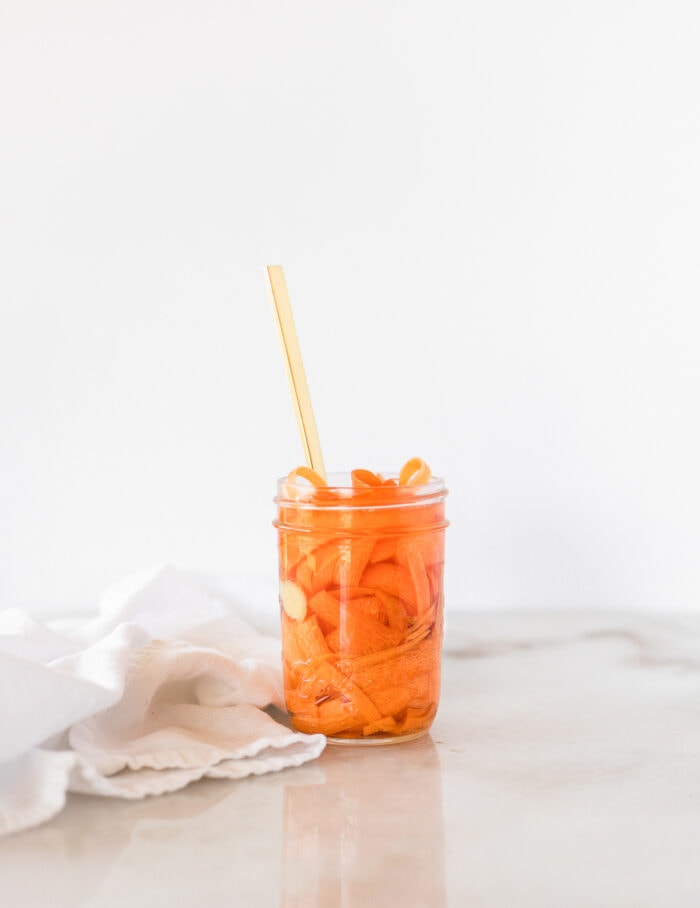 jar of pickled carrots with a gold fork in it and a white napkin beside it.