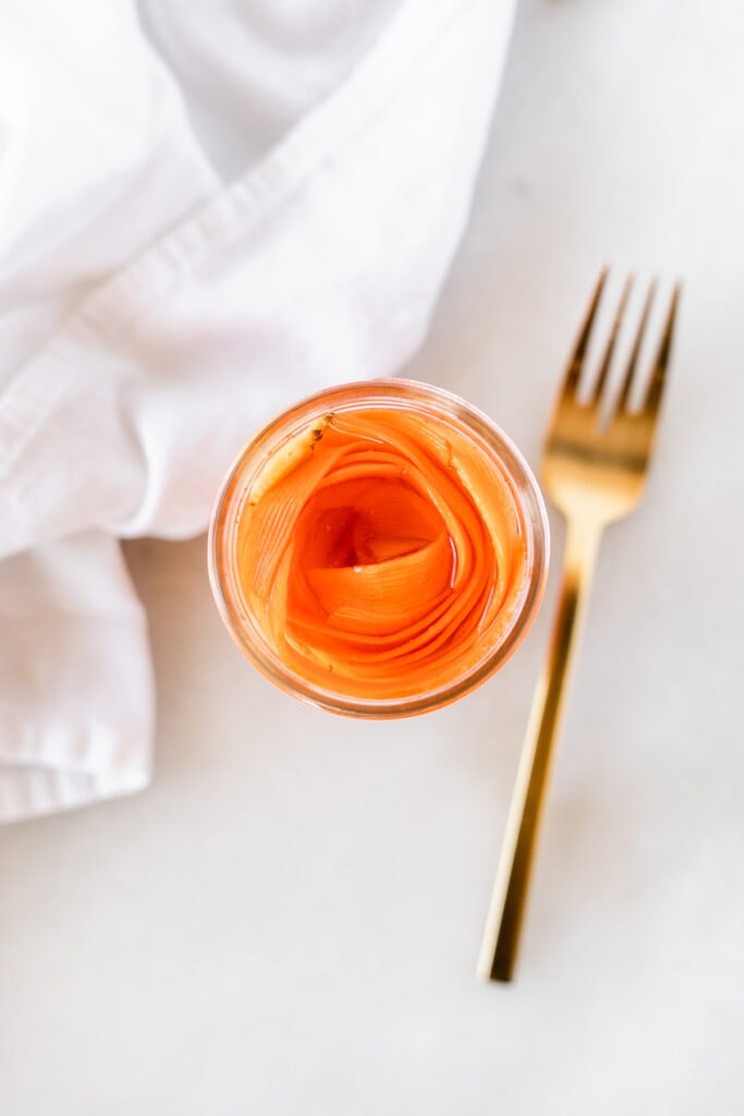 overhead view of pickled carrots in a jar with a gold fork beside it.