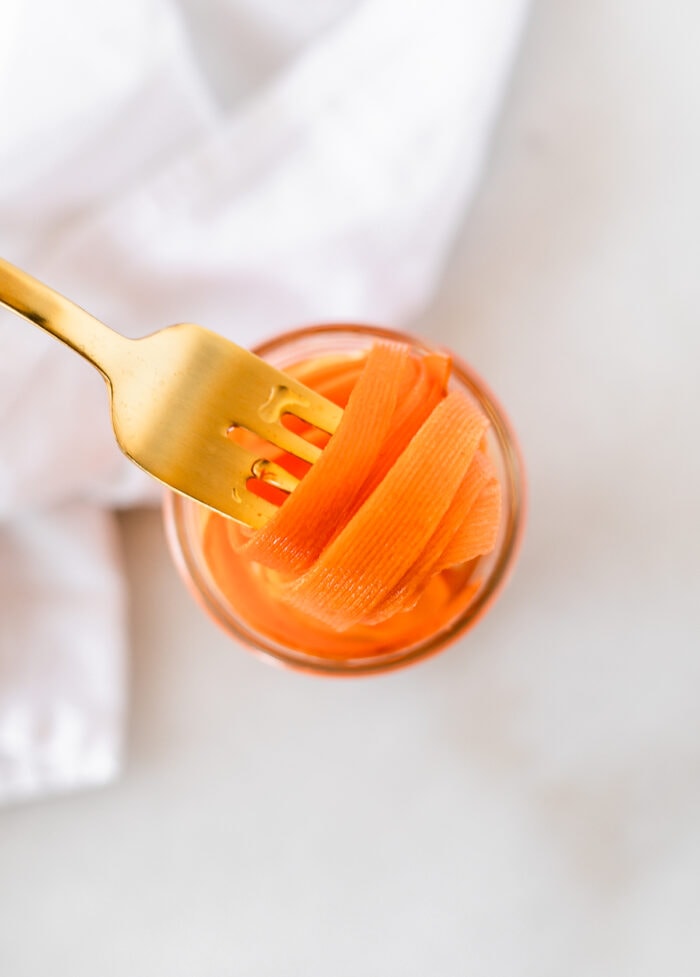 overhead view of a gold fork pulling pickled carrots from a jar.