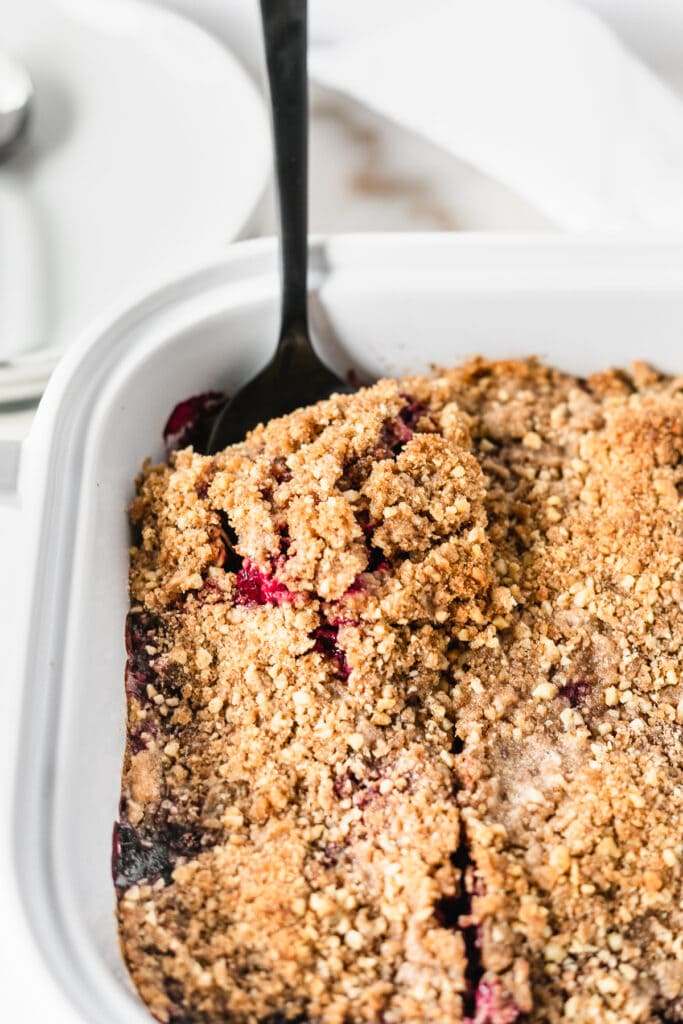 black spoon scooping out blackberry crumble baked oatmeal from a white baking dish.