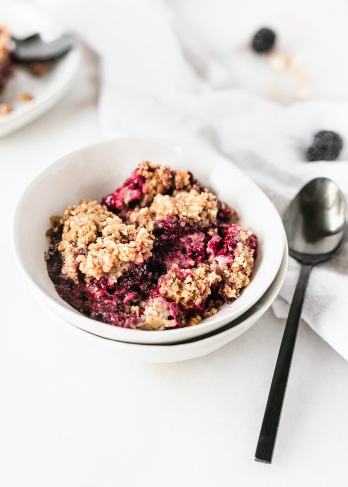 blackberry crumble baked oatmeal in a white bowl with a black spoon beside it.