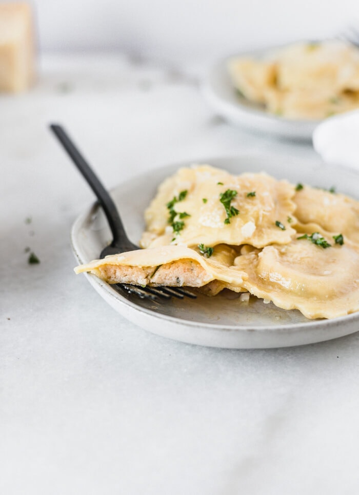 piece of lobster ravioli cut in half on a black fork sitting on a plate of ravioli.