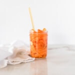 jar of pickled carrots with a gold fork in it and a white napkin beside it.