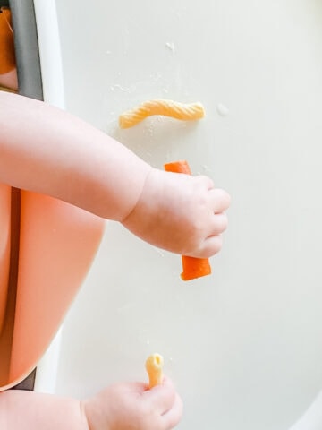 overhead view of baby hands gripping a carrot stick and a noodle.