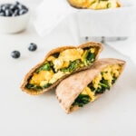 spinach egg and cheese breakfast pita halves stacked on top of each other with a bowl of blueberries in the background.