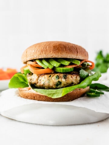 thai chicken and pork burger with avocado, pickled carrots and lettuce on a parchment covered plate.