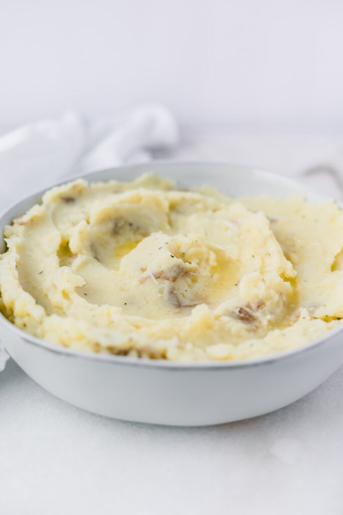 mashed potatoes with melted butter on top in a grey bowl with a white napkin behind it.
