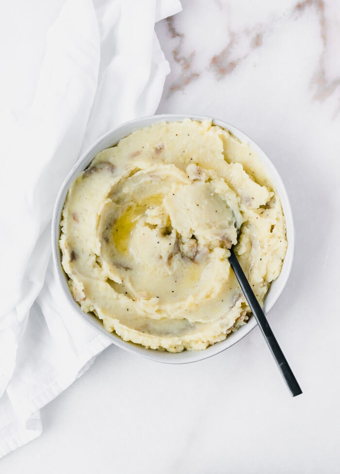 overhead view of mashed potatoes with melted butter on top in a bowl with a black spoon in it.