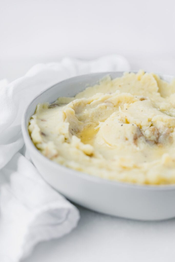 closeup of rustic mashed potatoes in a grey bowl with melted butter on top.