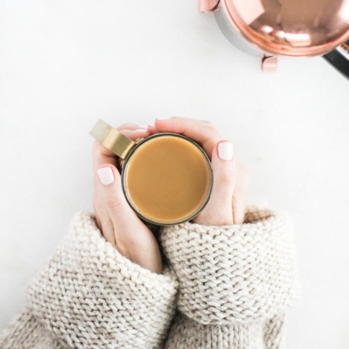 overhead view of hands around a cup of coffee with a copper french press in the corner.