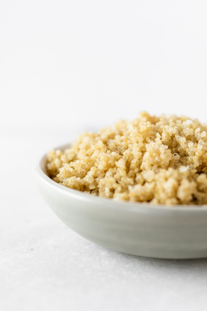 closeup of cooked quinoa in a small grey bowl on a white background.
