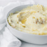 closeup of rustic mashed potatoes in a grey bowl with melted butter on top.