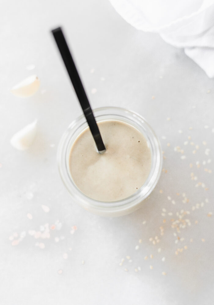 overhead view of a jar of tahini dressing with a black spoon in it.