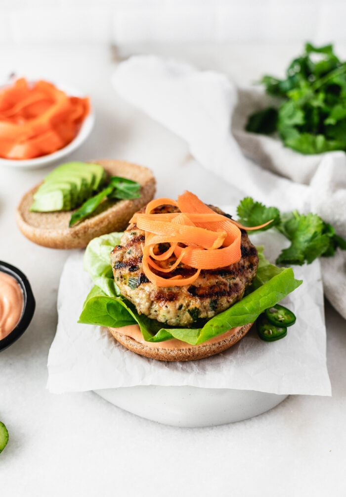 healthy thai burger on a plate topped with pickled carrots with the top bun behind it.