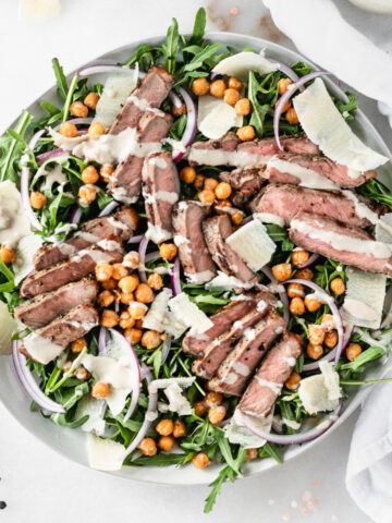 overhead view of steak chickpea arugula salad on a plate drizzled with tahini dressing.