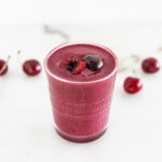 cherry berry probiotic smoothie in a glass with cherry halves on top.