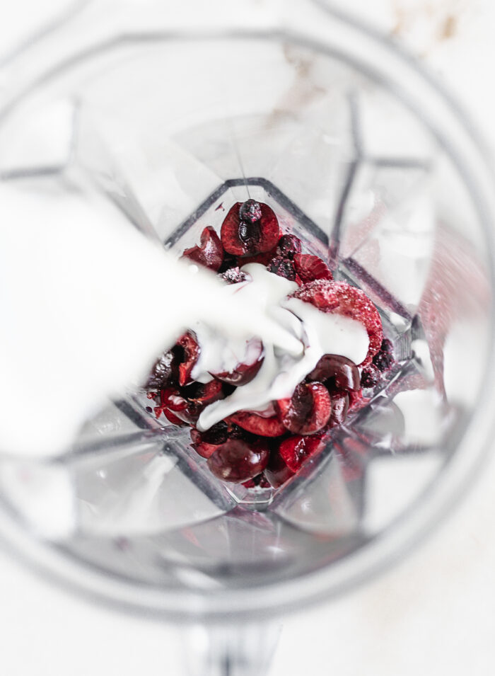 kefir being poured into a blender with cherries and frozen berries.