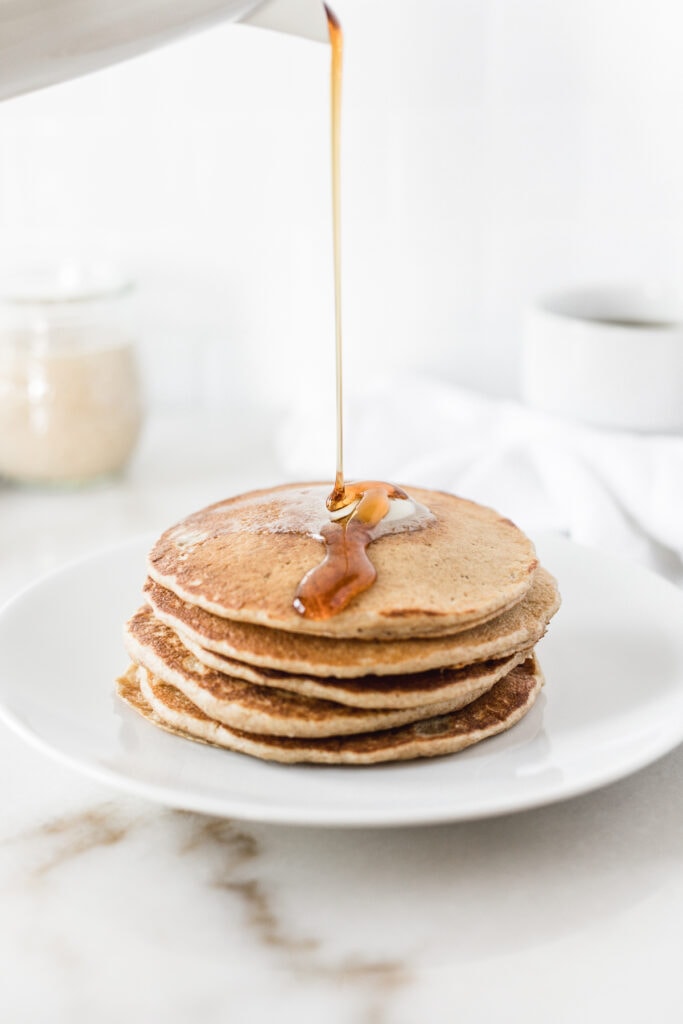 syrup being poured over a stack of sourdough discard pancakes on a white plate.