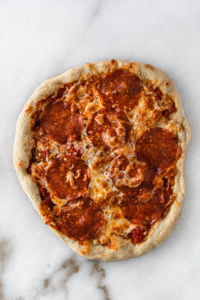 overhead view of pepperoni pizza on a white marble backdrop.