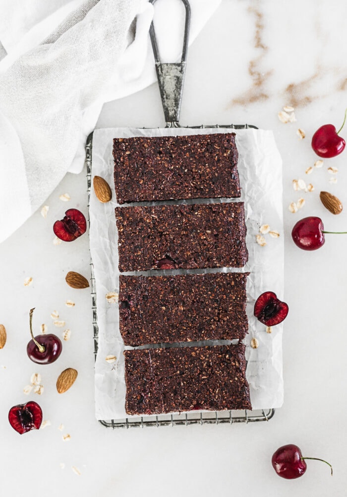 overhead view of cherry chocolate snack bars on a parchment lined wire rack surrounded by almonds and cherries.
