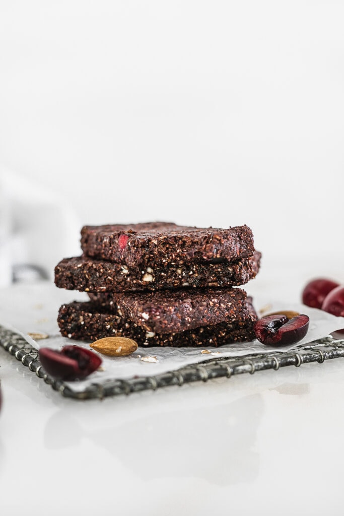 cherry chocolate snack bars stacked on top of each other surrounded by almonds and cherries.
