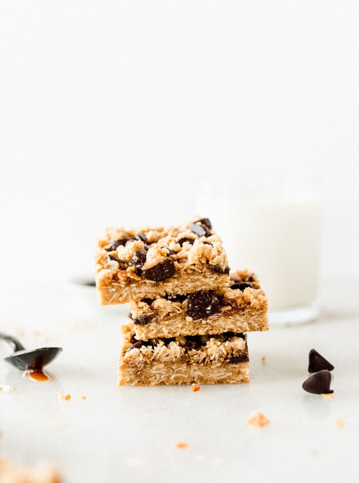three dream bars stacked with a spoon of caramel next to the and a glass of milk in the background.