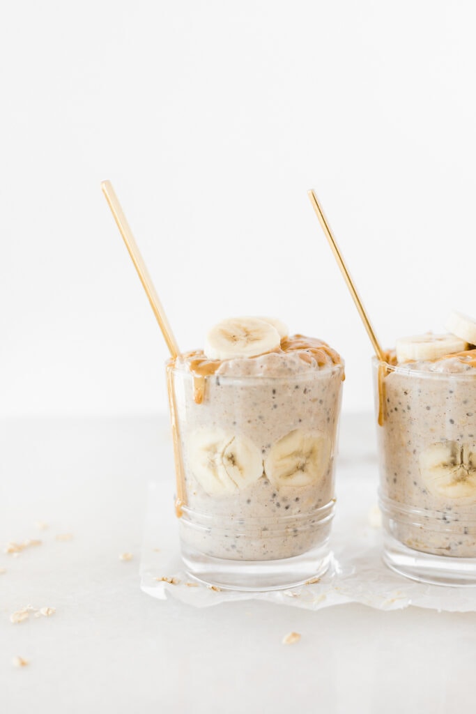 closeup of two glasses of peanut butter banana overnight oats with banana slices and peanut butter on top and gold spoons in them.
