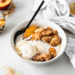 bowl of peach cobbler with ice cream on top with a black spoon in it.