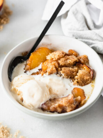 bowl of peach cobbler with ice cream on top with a black spoon in it.