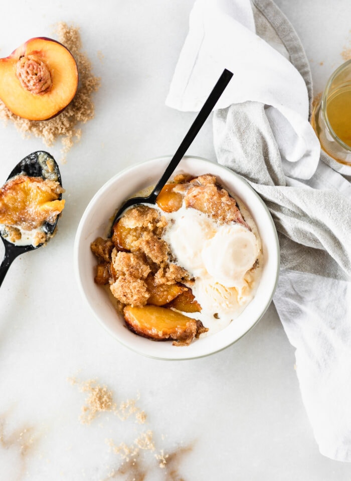 overhead view of bowl of peach cobbler with ice cream on top with a black spoon in it.