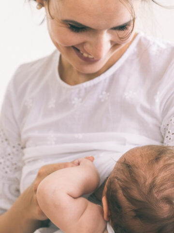 woman in a white shirt breast feeding a baby.