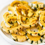 Closeup of roasted delicata squash half moons on a white plate.