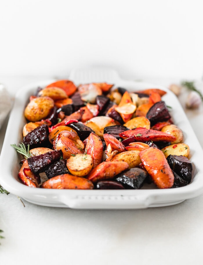 roasted root vegetables on a white platter with rosemary sprigs.